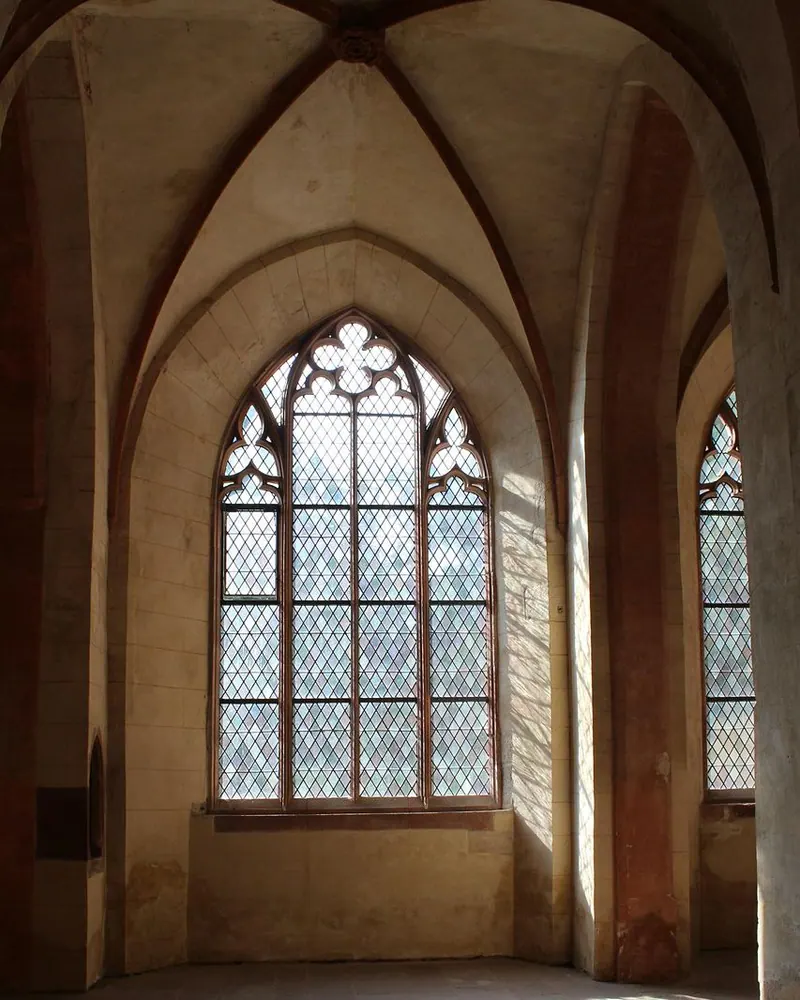 Hohes gotisches Spitzbogenfenster mit Sprossenverglasung in einem Steinraum, Sonnenlicht fällt auf den Fliesenboden